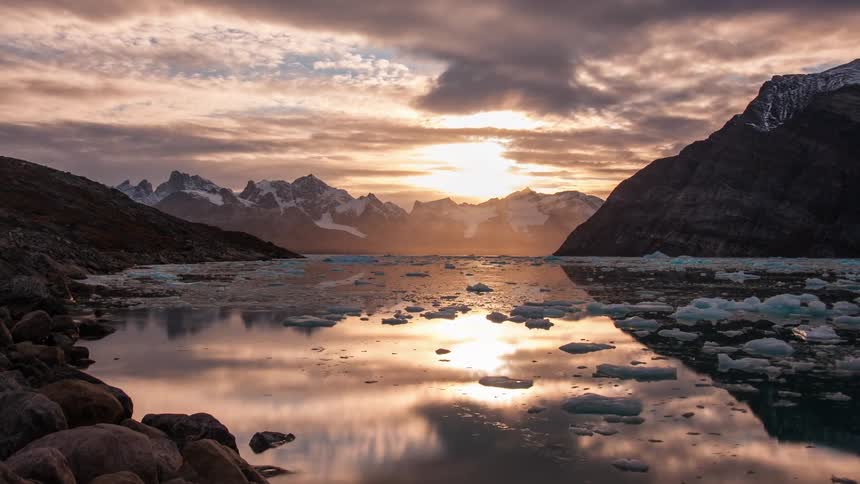Chunks of ice float across the surface of a river as the sun sets and landscape is engulfed in darkness