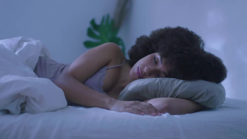 A woman in a bedroom sleeping on a bed with a pillow and sheets