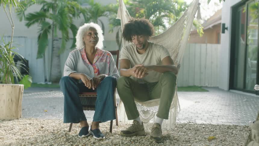A grandmother and her grandson sitting outside on a porch in a backyard laughing and talking to each other at daytime