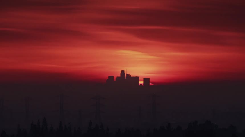 Silhouettes of utility towers and buildings as the sun sets in an orange and red sky