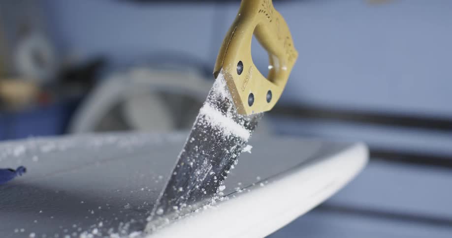A saw sticking out of the surface of a surfboard inside a workshop