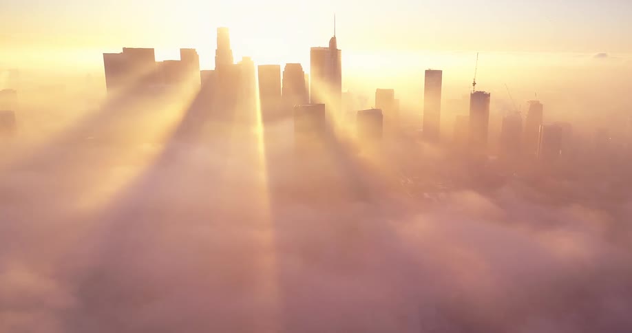 Building silhouettes with sun rays shining through in a bright orange sky with a smokey atmosphere