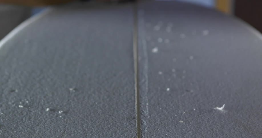 A man sanding the surface of a surfboard in a workshop