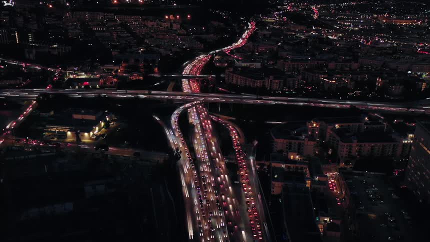 Vehicle headlights drive by in a blur as traffic passes down the freeway at night in a city