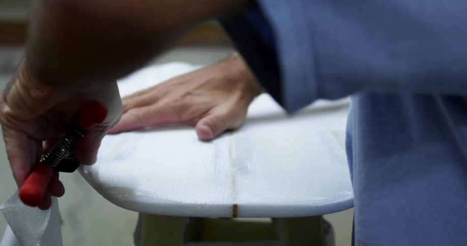 Man uses scissors to cut white fabric covering a surfboard