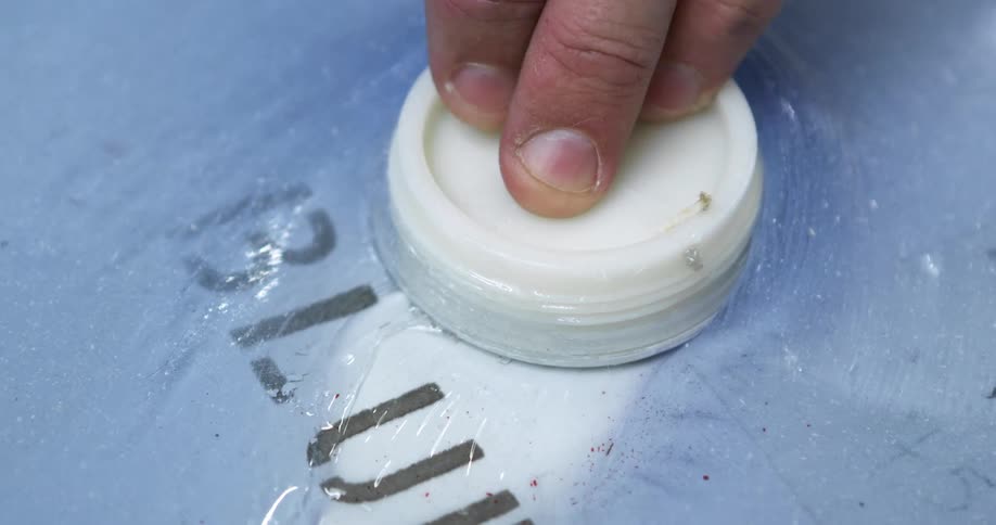 A human hand presses three fingers against a circle white piece of plastic and moves it across a thick blue gel