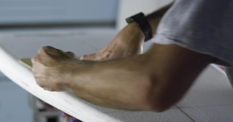 A man marking measurements over a surfboard with a pencil