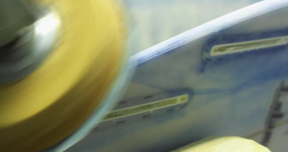 A person sanding the edge of a surfboard with a power tool in a workshop