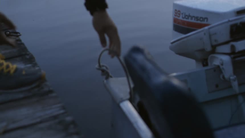 A person unties a small boat from a dock in the morning