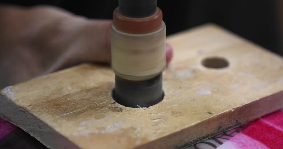 A man uses a sander to smooth the inside of a hole drilled in a piece of wood
