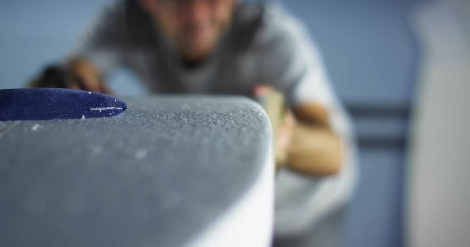 A man working on sanding a surfboard at a shop
