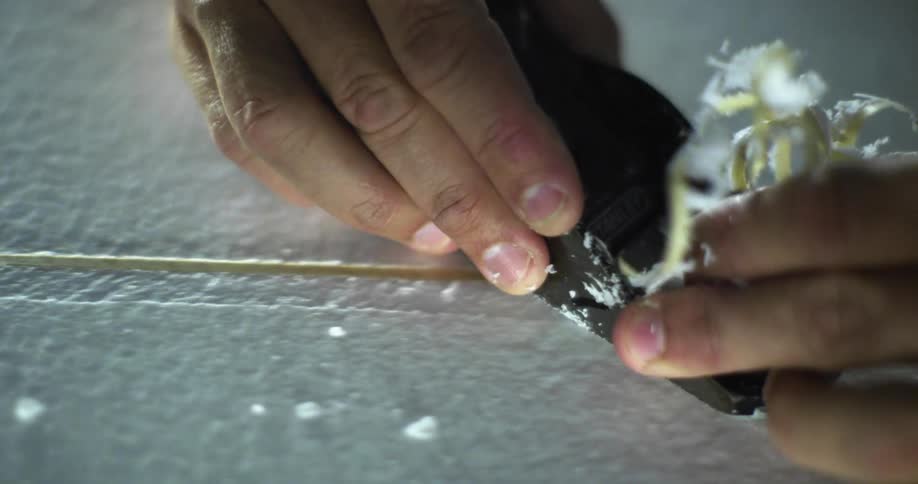 A man using a tool to carve a slit in the surface of a surfboard