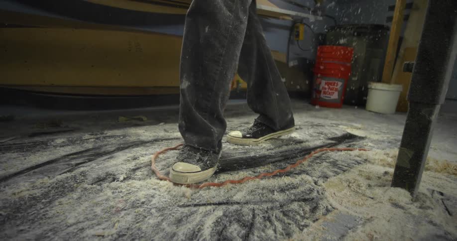 A workshop floor covered in sawdust as more falls from a workbench