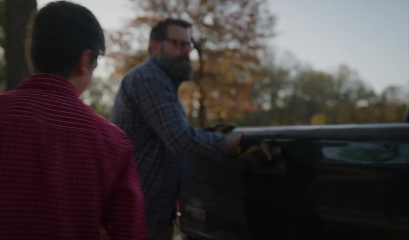 Son helps father unload logs from truck bed near fence