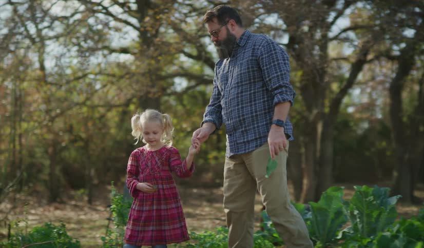 A man holds a little girls hand and points things out to her as they walk through a garden