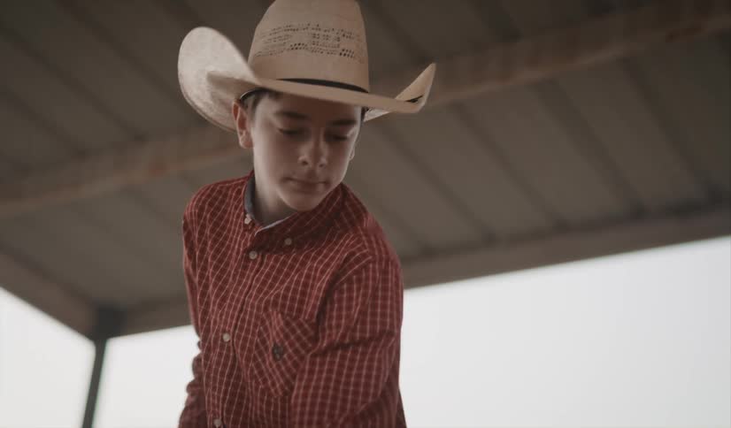 A boy in a cowboy hat uses a pitchfork to separate and move hay