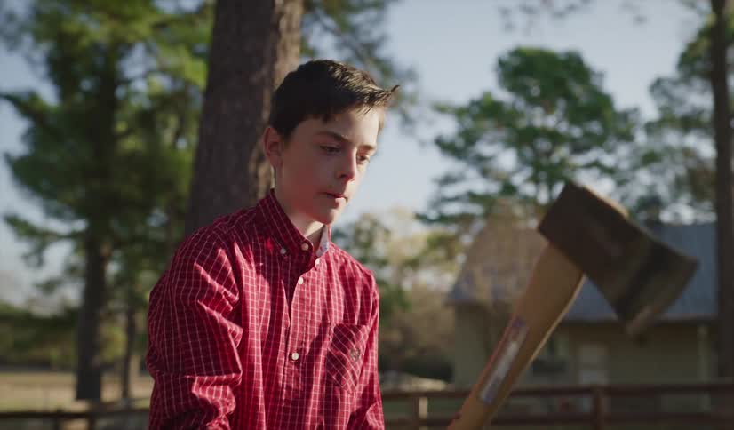 A man watches as his son places a piece of wood on a tree trunk and lowers an ax to chop it