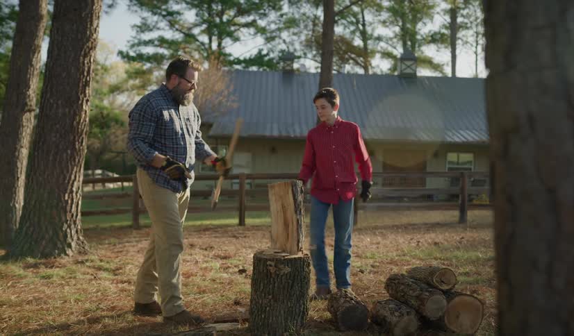 Father with glasses and beard shows his son how cut wood with ax