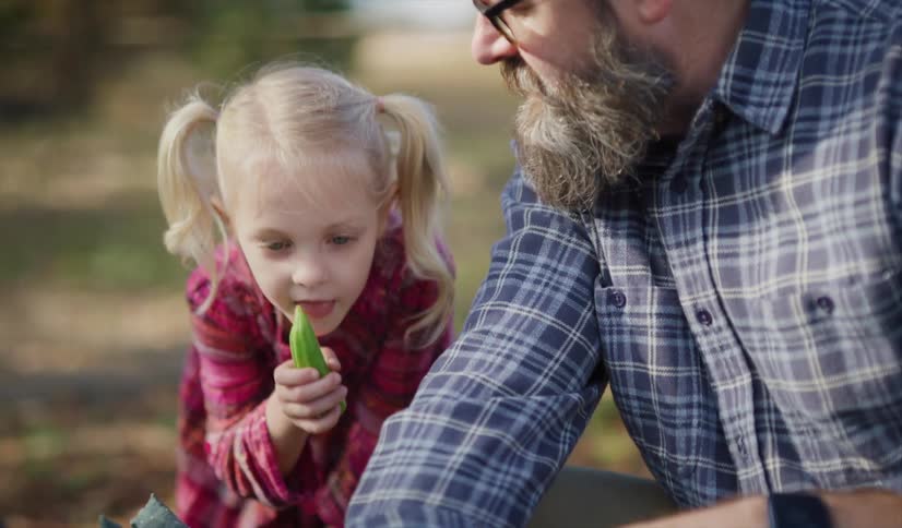 Father and daughter outdoors kneeling down in front of a broccoli plant and talking during the day