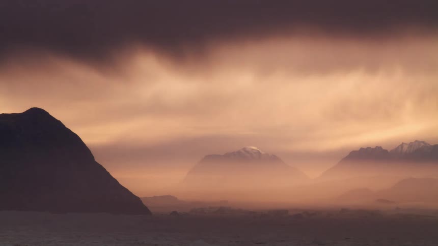 Mountains under a darkening orange sky with a smokey atmosphere