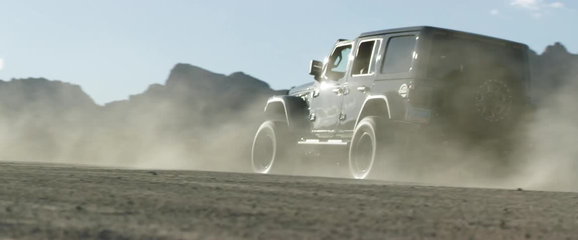 Jeep turns on road kicking up dust and driving toward mountains