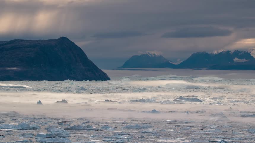 A lake with water and ice with a mountain range the sky and clouds in the background