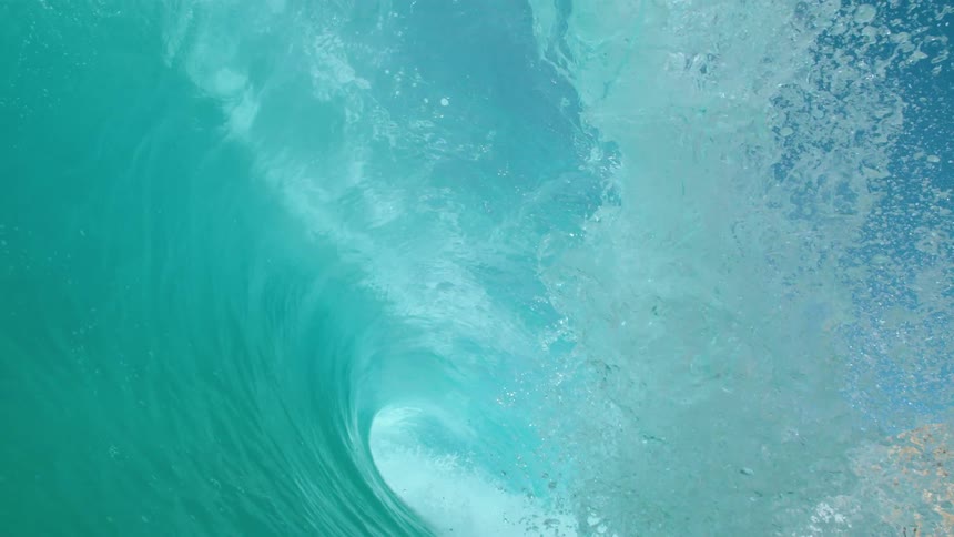 Big blue wave splashes as it rolls overhead on a clear day