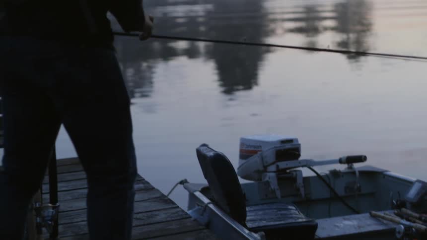 A man places rods on a boat tied to a pier