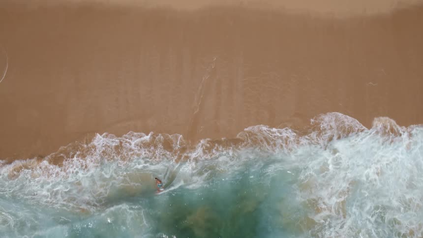 Overhead view of a skimboarder catching a wave at the beach