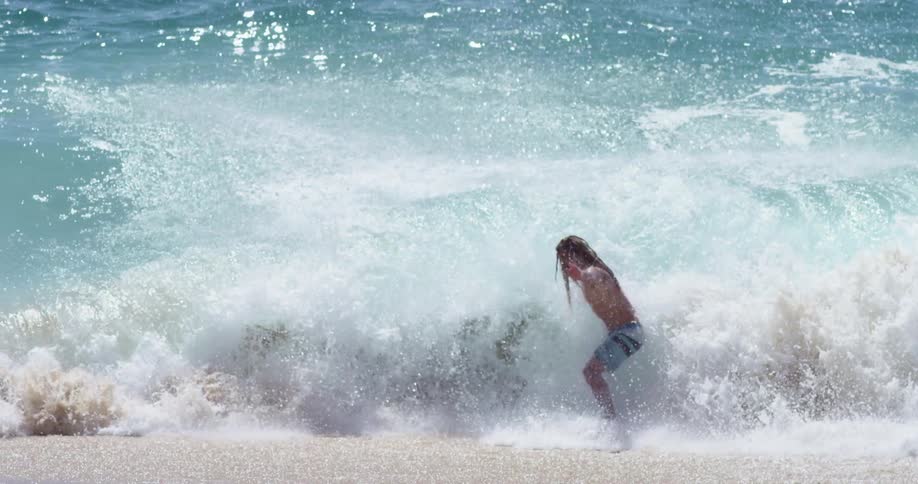 Surfer rides a big blue splashing wave into the beach