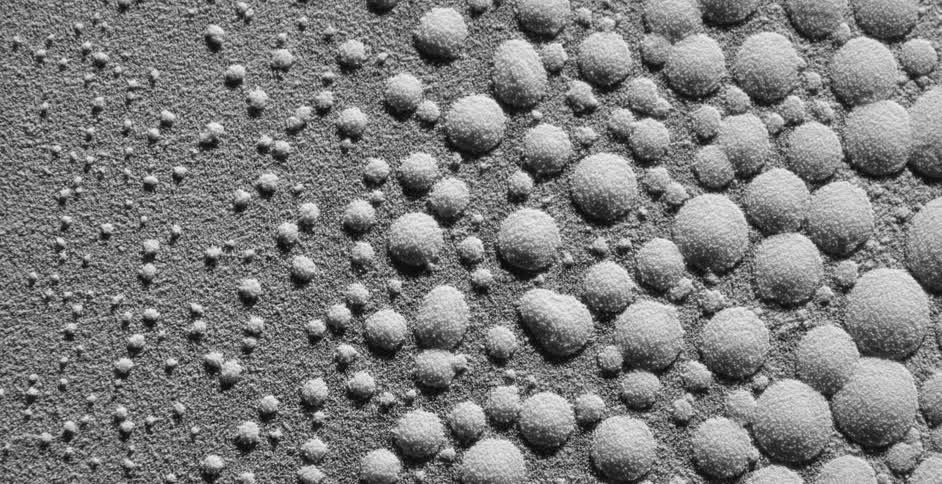 Drops of water covered in white dust move and shatter over a vibrating surface