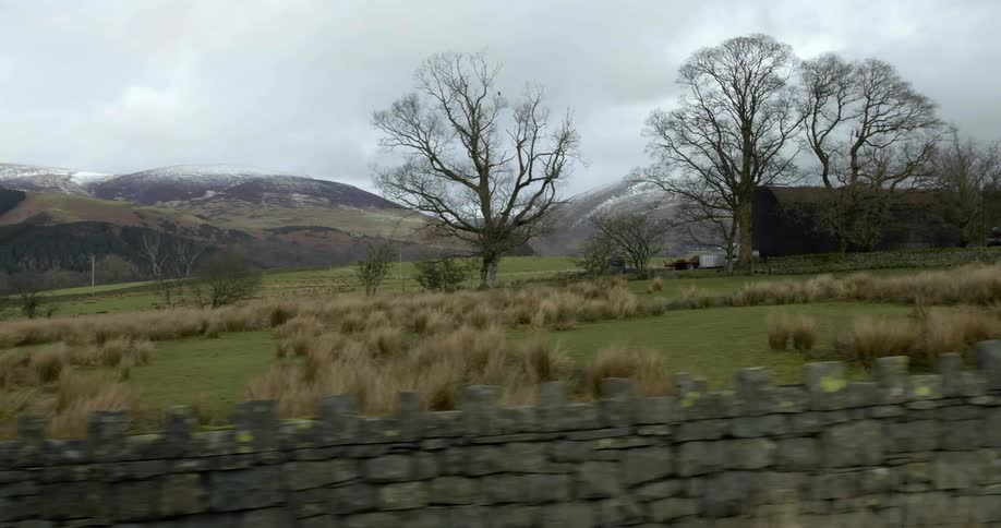Stone wall in front of green grass fields in the countryside near the mountains on an overcast day