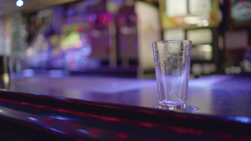 An empty beer glass on a bar counter with liquid still dripping down the insides
