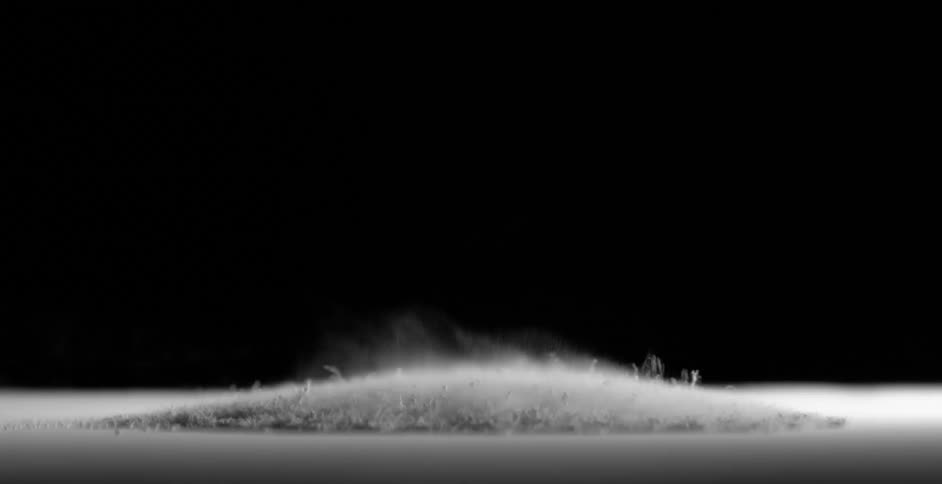Gray powder vibrating up and down on a surface in a black room