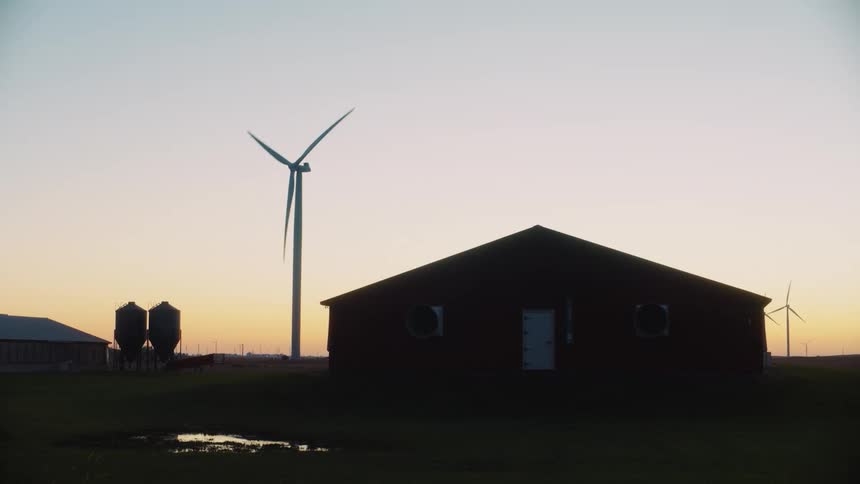 Silhouette of a wind turbine near a shack on a field at sunset
