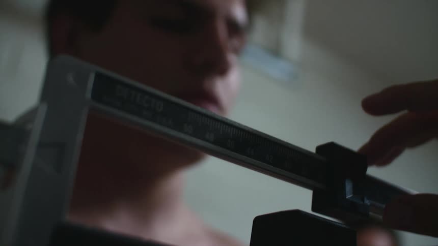 A man in a room standing on a scale being weighed with a wall in the background