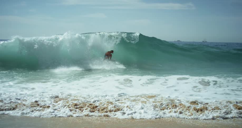 A person on a beach surfing on a surfboard on a wave with the sky and clouds in the background