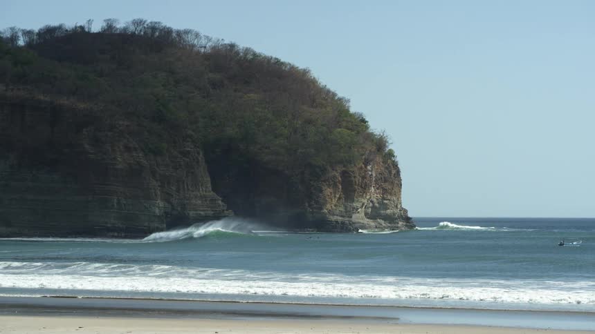 Waves roll in on a beach near a high land promontory under a clear sky