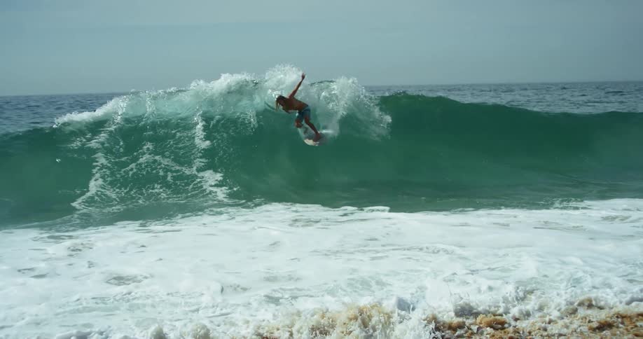 Surfer rides a big blue wave into the beach