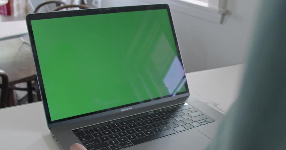 A person in a room using a laptop on a table with a wall and window in the background
