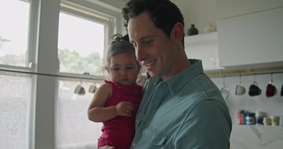Father holds her daughter and makes a video call in the kitchen