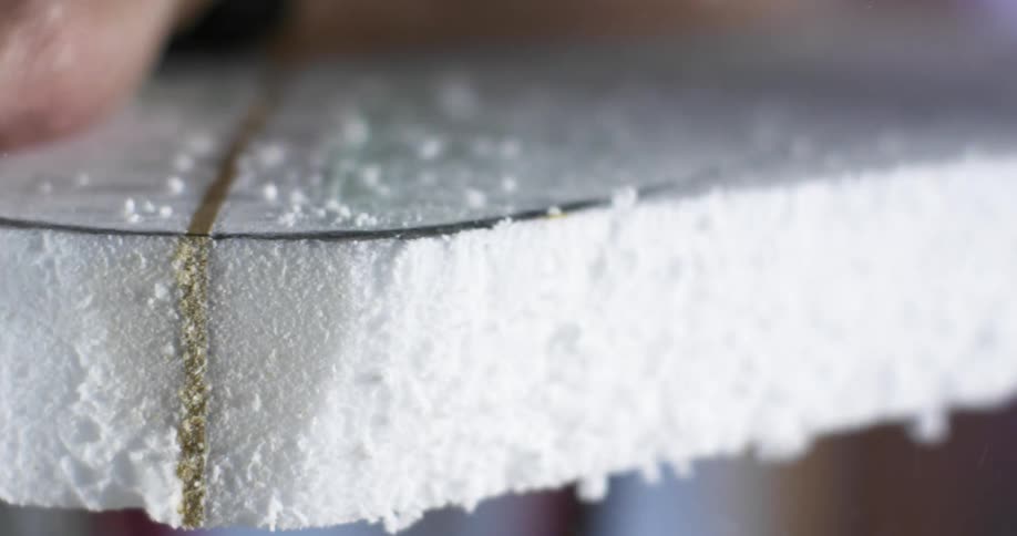 A hand holding a saw cuts off pieces of excess foam on the edge of a foam object