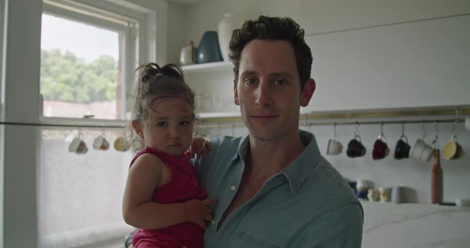 A man stands in a kitchen holding his young daughter smiling proudly