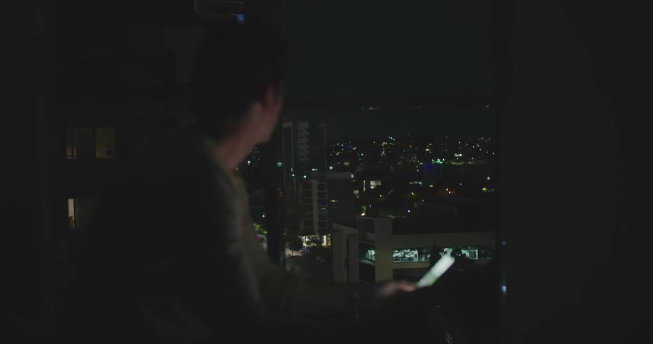 A man sitting in a room next to a window looking at a smart phone