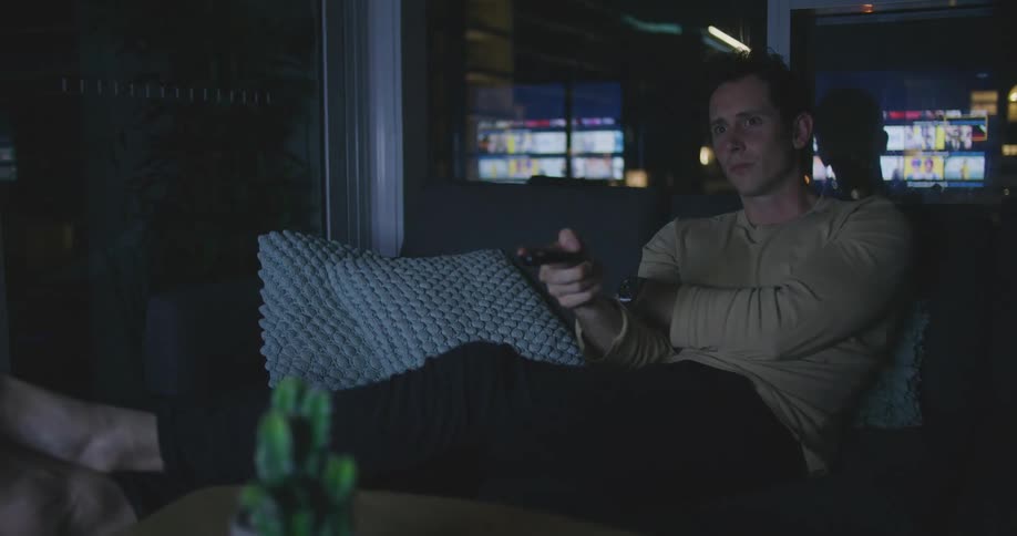 Man sitting on a couch in a living room with his feet up scrolling through options on a television at nighttime