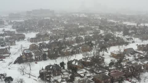 Snow falls onto a foggy residential neighborhood during the day