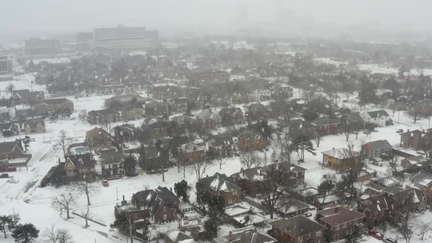 Snow falls onto a foggy residential neighborhood during the day