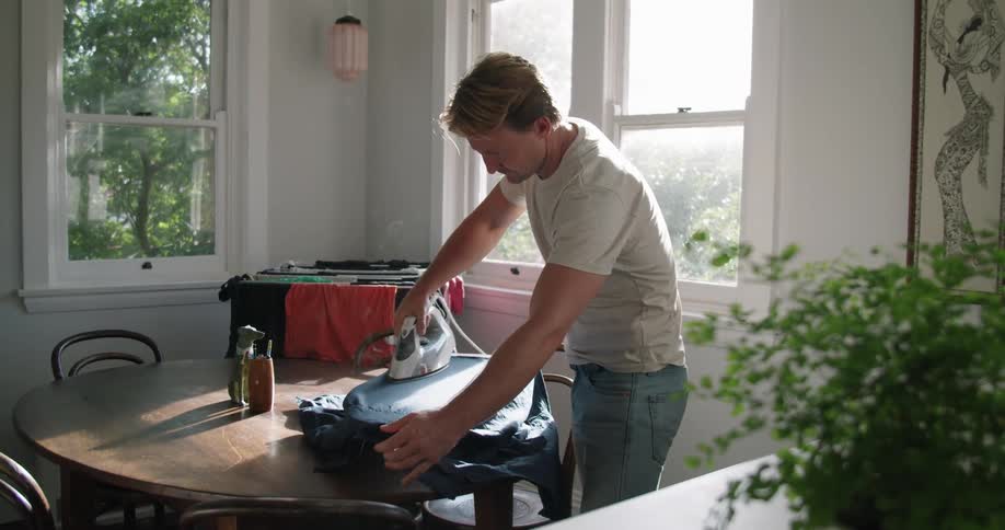 A man at home irons a shirt