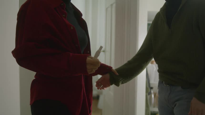 A man grabs his wife arm and goes in for a hug as she holds a pregnancy test outside the bathroom