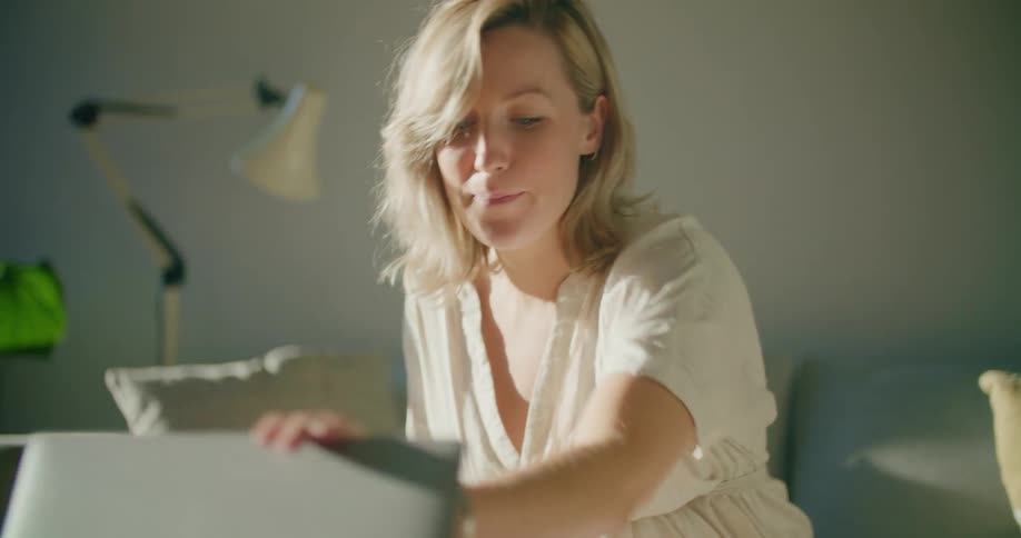A pregnant woman sitting on a couch and closing a laptop on a table